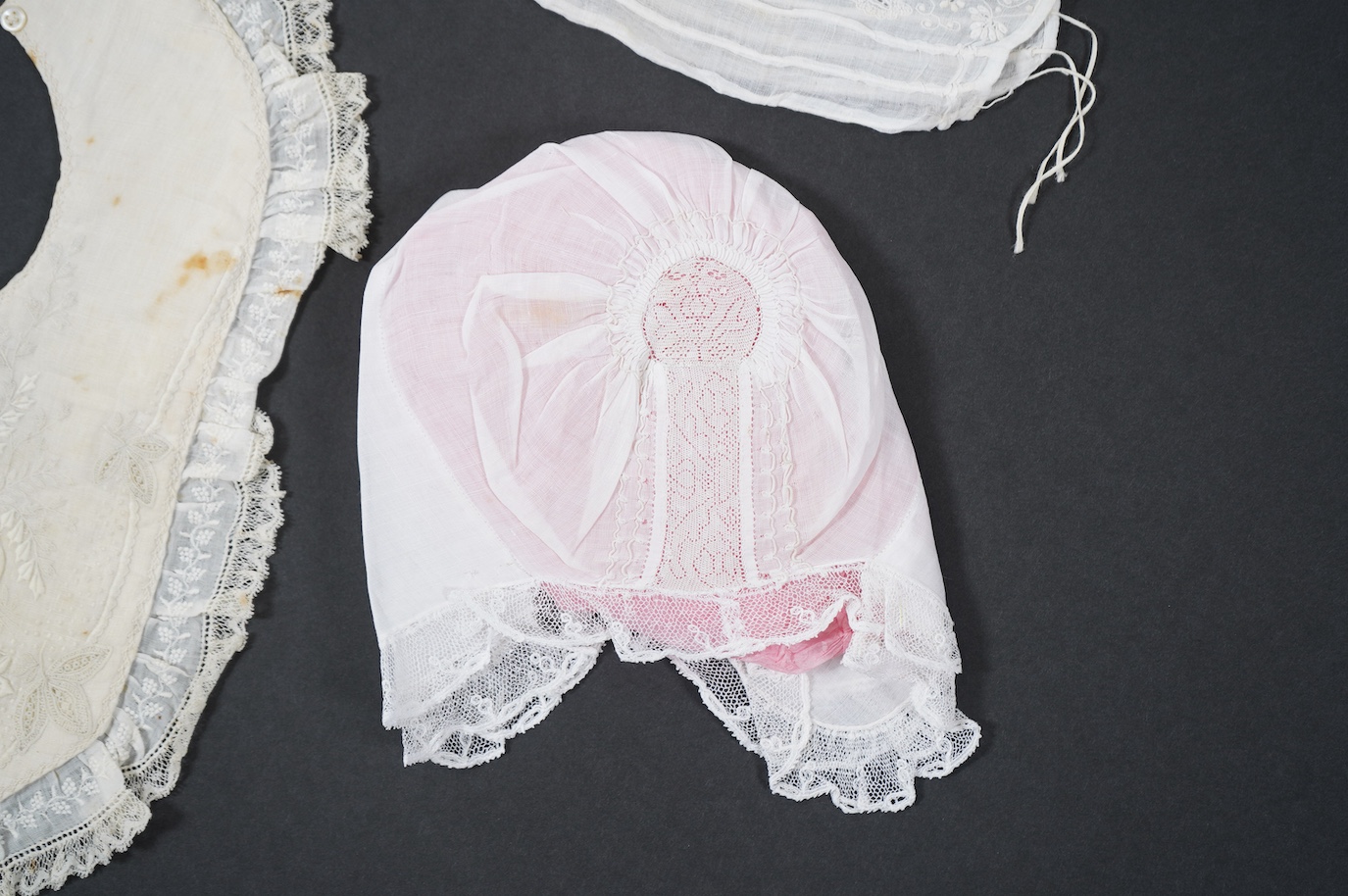 An 18th century Holly Point needle lace panelled linen baby bonnet, an early 19th century white worked baby bib and bonnet and a later 19th century finely ruffed lace bonnet (4). Condition - Holly Point bonnet and bib ha